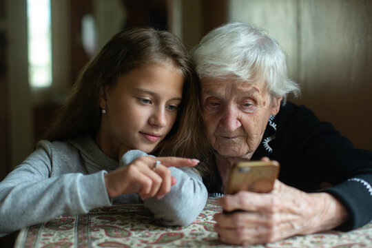 A teengirl teaches her grandmother how to use a smartphone. The warm moment shows care, connection, and the bridge between generations through technology.