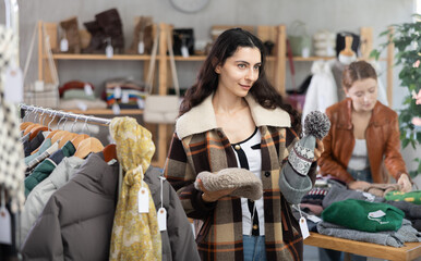 Armenian woman customer browsing goods and choose search warm hat in store, buyer consider some items. Concept of seasonal wardrobe shopping. Style and fashion type look, modern trends
