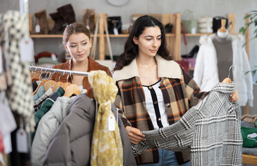 Obraz premium Two young women choosing outerwear for autumn and winter in clothing store