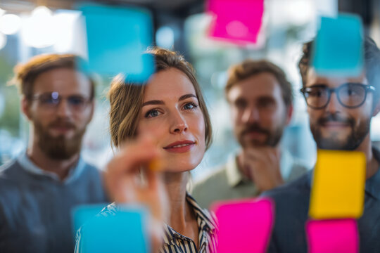 A diverse team collaborating and brainstorming together using colorful sticky notes on a glass board during a creative office meeting session