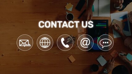 A dynamic overhead view of a team exploring various contact methods with graphic icons on a wooden desk, emphasizing modern communication in the workplace. Raster - Powered by Adobe