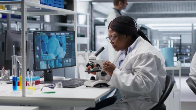 African american woman analyzing molecular samples in a bio lab, using professional microscope. Healthcare and biochemistry experiments represent scientific method and discovery. Camera B.