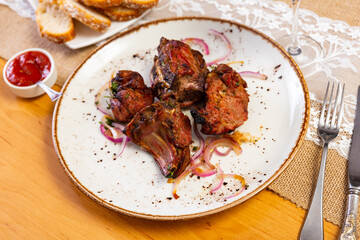 There is plate with cooked mutton barbecue shashlik on wooden table. Pieces of lamb fried on open...
