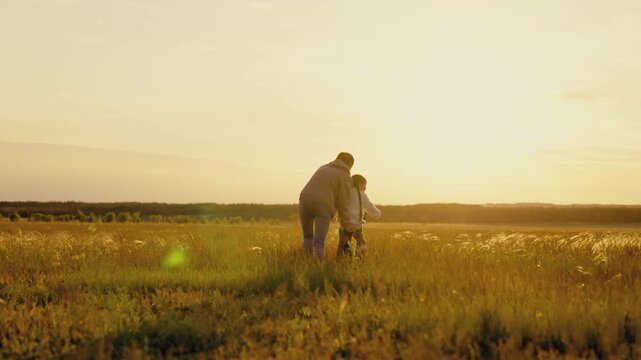 Child girl riding bike with her mom in meadow. Mom teaches her little daughter to ride bike on grass in park. Mother teaches her child to keep his balance while riding bike. Family game Mom kid pedal