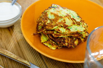 Delicious zucchini pancakes with bowl of sour cream served on plate