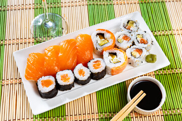 Sushi set con maki with uramaki rolls and salmon nigiri is served in white narrow rectangular plate. Traditional Japanese Asian cuisine, gastronomy tourism