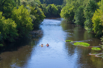 Two canoes and kayaks paddle along a river lined with forest