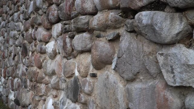 A panoramic view of the weathered, boulder-built walls of Dobele Castle ruins (Latvia) under a dramatic sky. Salt deposits on the facade highlight the ancient nature of this medieval building complex.
