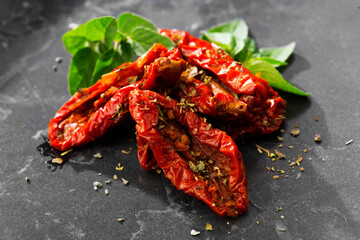 Sun dried tomatoes with aromatic herbs, oregano, marjoram leaf. Over black stone background, close up. Italian cuisine, healthy vegan food, Mediterranean diet. Dry tomato. 