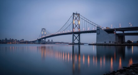 Suspension bridge illuminated at dusk over calm water with city
