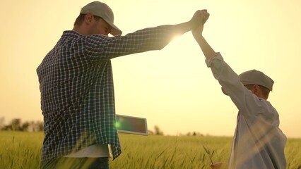 Father son handshake, Dad child walk together on wheat plantation in summer. Family business, farmers. Happy family, Farmer father works with tablet in green wheat field with his little son. Dad, son