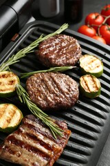 Electric grill with beef steaks, zucchini and rosemary on black table, closeup