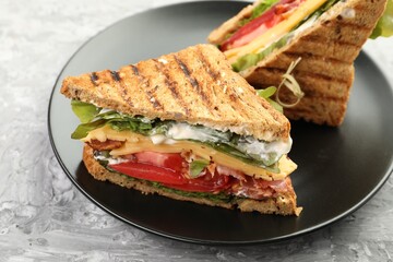 Tasty sandwiches with bacon, cheese, vegetables and sauce on grey textured table, closeup