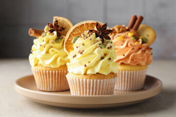 Delicious cupcakes with colorful cream, spices and nuts on grey table, closeup