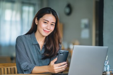 Obraz premium Beautiful young Asian woman using a laptop and smartphone at a desk in a room