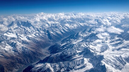 Fototapeta premium Panoramic aerial view of rugged snow covered mountain range with dramatic clouds and blue sky, evoking awe and tranquility