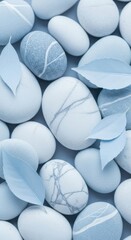 A closeup, topdown view of smooth, light bluegrey pebbles and a few delicate blue leaves, creating a serene and calming texture