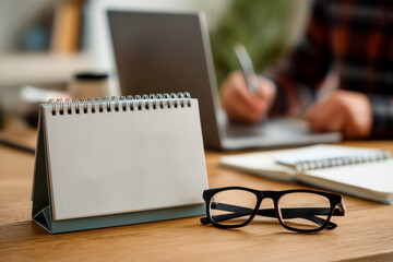 A desk calendar is placed on a wooden desk with a laptop and glasses nearby