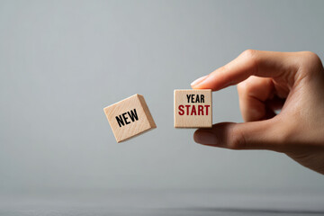 Hand holding wooden blocks with new year start text against gray background