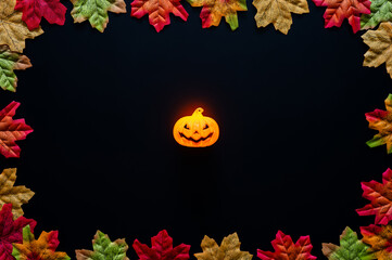 Jack o lantern with orange light puts on black background with maple leaves for Halloween holiday background.