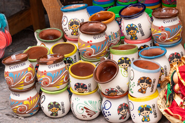 A collection of colorful ceramic cups with various designs and patterns, including one with a woman . Historic center of Querétaro, colonial architecture, decorations for the celebration of Mexico's I