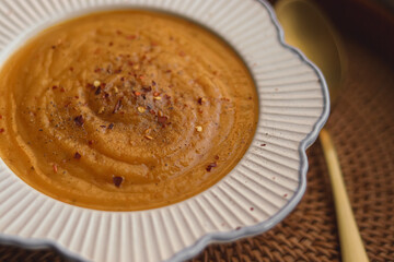 Creamy orange vegetable soup, garnished with red chili flakes. Warm healthy comfort food serving in a round bowl