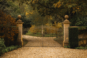 Wrought iron gates closing a gravel driveway leading to a secluded autumn estate. Cotswolds...