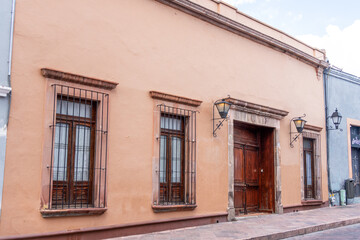 A brown building with a wooden door and windows. The building is old and has a rustic feel. Historic center of Querétaro, colonial architecture, decorations for the celebration of Mexico's Independenc