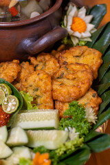 Close-up of crispy Indonesian corn fritters (bakwan) served on banana leaf with cucumber and parsley garnish — traditional snack/party platter