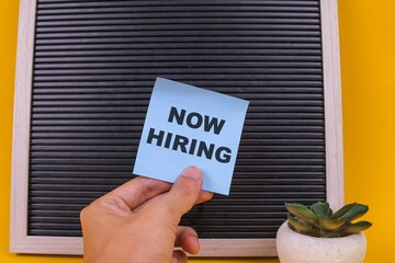 Hands Holding Notes With Now Hiring Text Over Blank Black Board