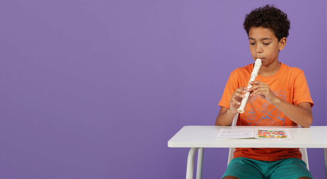 A young student learning to play the recorder at his desk. Child practicing a wind instrument for a music lesson. Education and childhood development concept with copy space