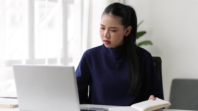 Young Asian businesswoman taking notes from laptop.
