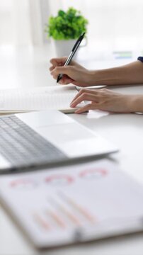 Professional businesswoman analyzing business charts while writing notes and pointing at laptop screen during strategic planning session.