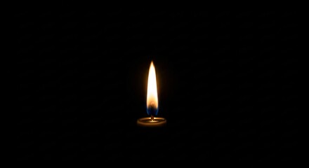 A single candle flame burns brightly against a stark black background casting a warm glow