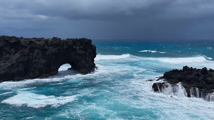 Volcanic rock arch over teal ocean waves, storm clouds gathering