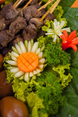 Close-up of a carved vegetable garnish (carrot and cucumber flower) on a festive Indonesian food platter with telur pindang and seasoned meat