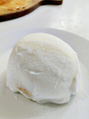 Close up of a Single Creamy White Milk Bun Dusted with Sweet Powdered Sugar on a Plate