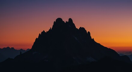 Dramatic silhouette of a jagged mountain range is cast against a colorful twilight sky, displaying vibrant hues of purple, orange, and yellow during the magical hour.