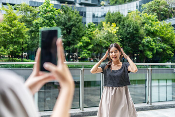 Two cheerful beauty asian friends celebrate friendship and creativity by live streaming their fun dance routine on social media in a vibrant city park, vlogger influencer content creator enjoy and fun