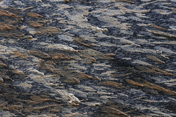 Close up view of natural gray and brown rock texture background. This rough stone surface shows layered geological pattern with solid and earthy character