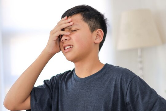 Stressed Asian Teen Boy Suffering from Painful Headache or Migraine While at Home