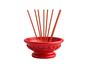Red incense bowl with brown sticks radiating upwards against a stark black background