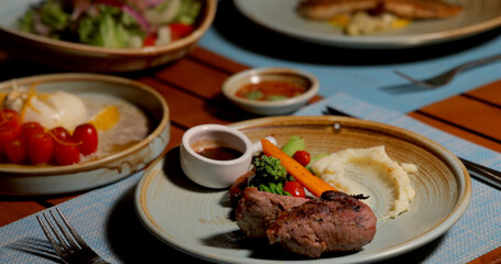 Plated steak dinner with vegetables, mashed potatoes in cozy restaurant setting. Fine dining, gourmet meal, culinary presentation, inviting atmosphere.