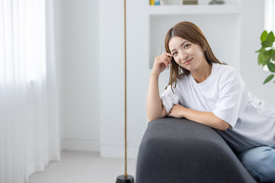 Woman sitting on sofa and relaxing in bright living room with natural light - Powered by Adobe