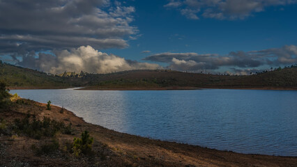 A beautiful lake with hilly shores. The evening golden hour. Glare, ripples on the surface of the water. The clouds in the blue sky are highlighted. Madagascar. Lake Mantasoa.