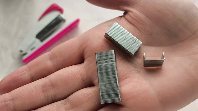 Metal staples in a woman's hand, stapler on a table