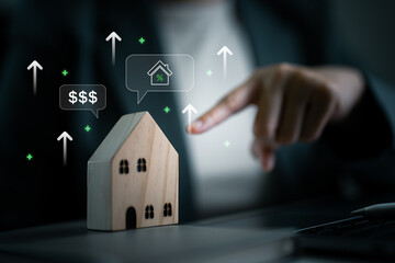 Hand pointing at wooden house with rising arrows, percentage and dollar signs. Represents increasing interest rates, property value, mortgage cost and housing market trends.