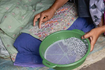 Close-up of a Bangladeshi village woman's hand placing shiny beads onto fabric (kameez). Rural housewife working on handicrafts for income, showcasing poverty and small business.