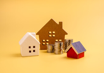 Home investment and property finance concept with model houses and stacked coins on yellow background, symbolizing real estate value, housing market growth, mortgage planning, and financial strategy.