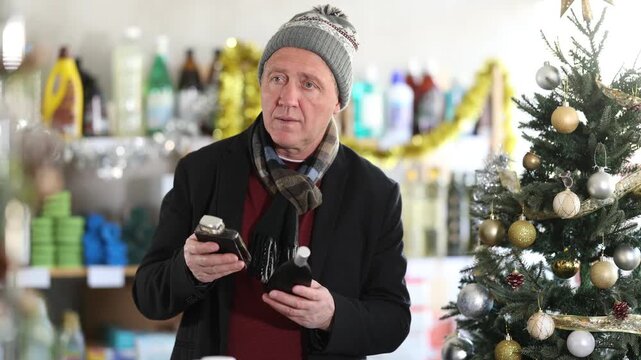 In X mas, senior man sniffs fragrance of perfume, choose scent spray with pleasant smell. Customer pulverize perfume, chooses toilet water. Client sprays perfume, snuff it and chooses perfume